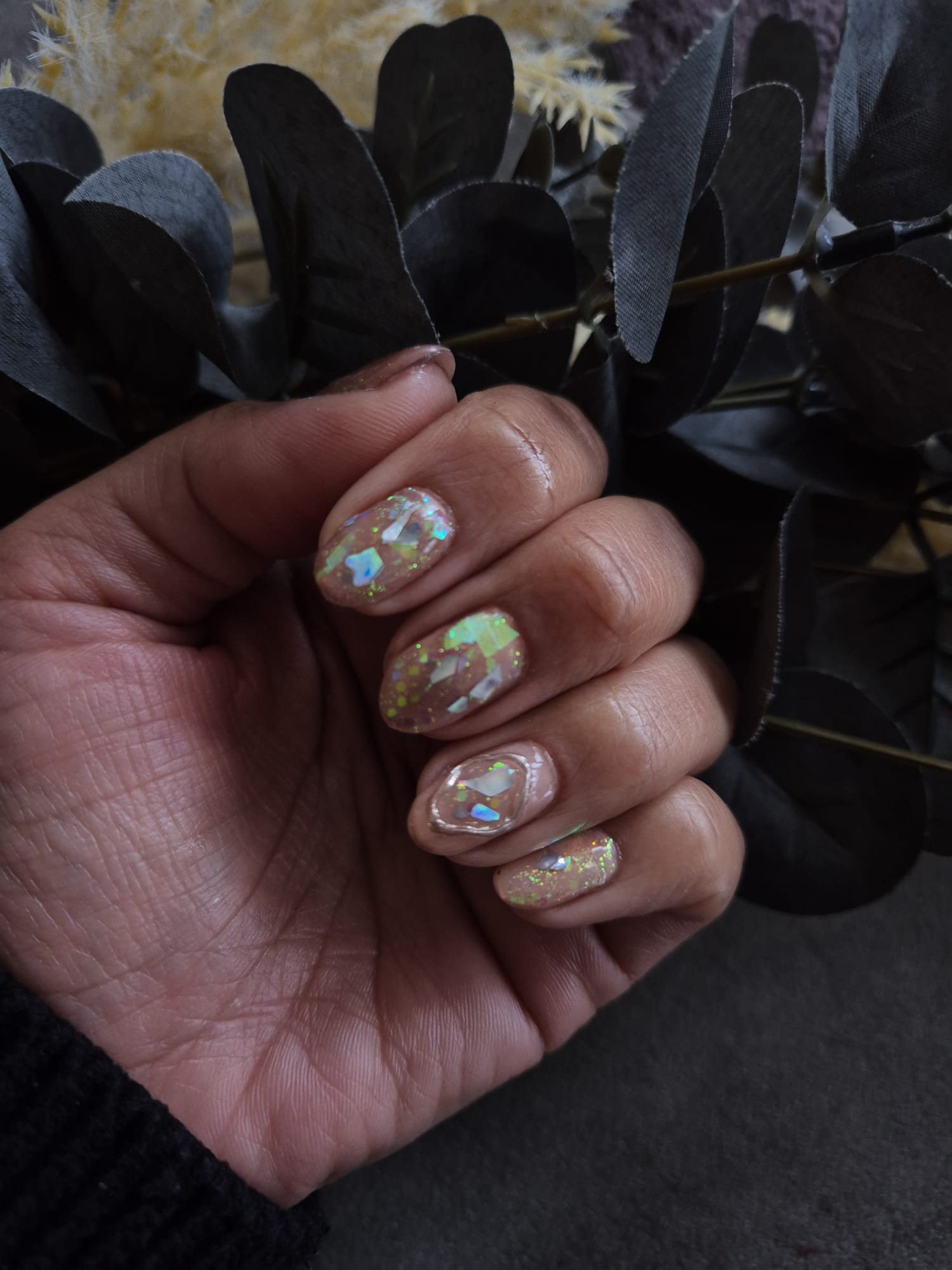 Opal glass-shard glitter nails against dark foliage